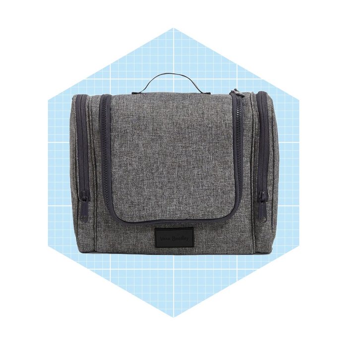 A gray toiletry bag sits upright on a light blue grid background, featuring a top handle and multiple zipped compartments.