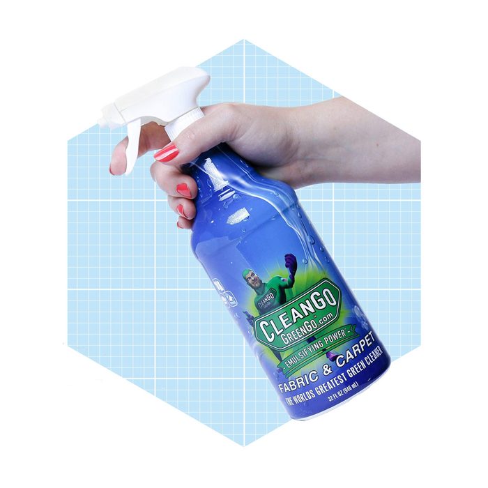 A blue spray bottle is held by a hand, ready to clean fabrics and carpets, set against a light blue grid background.