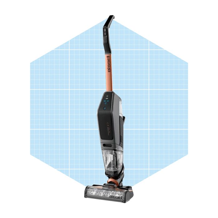A sleek vacuum cleaner with a transparent dirt container stands upright against a light blue grid background, indicating a modern design with digital controls.