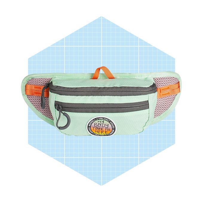 A mint green waist bag with zippers and a circular patch, positioned on a light blue grid background, is designed for carrying small items conveniently.