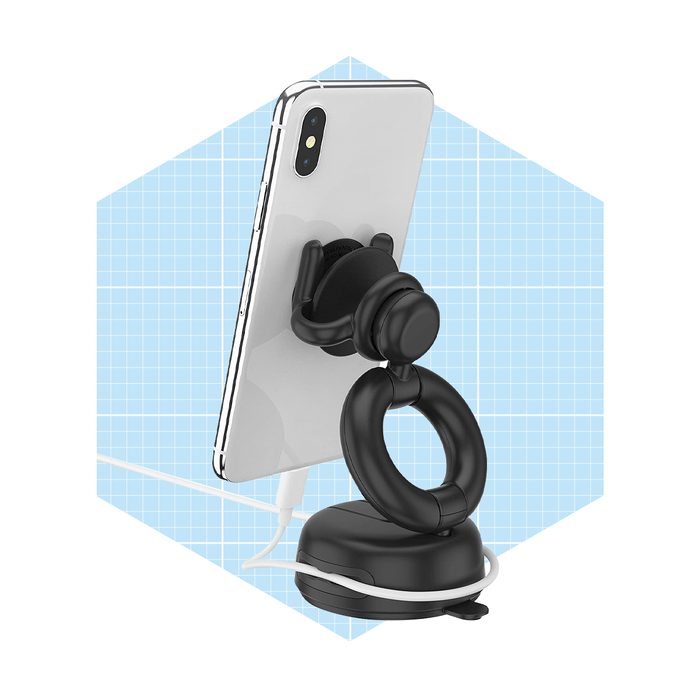 A smartphone is mounted on a black holder, charging via a cable, set against a light blue, grid-patterned background.