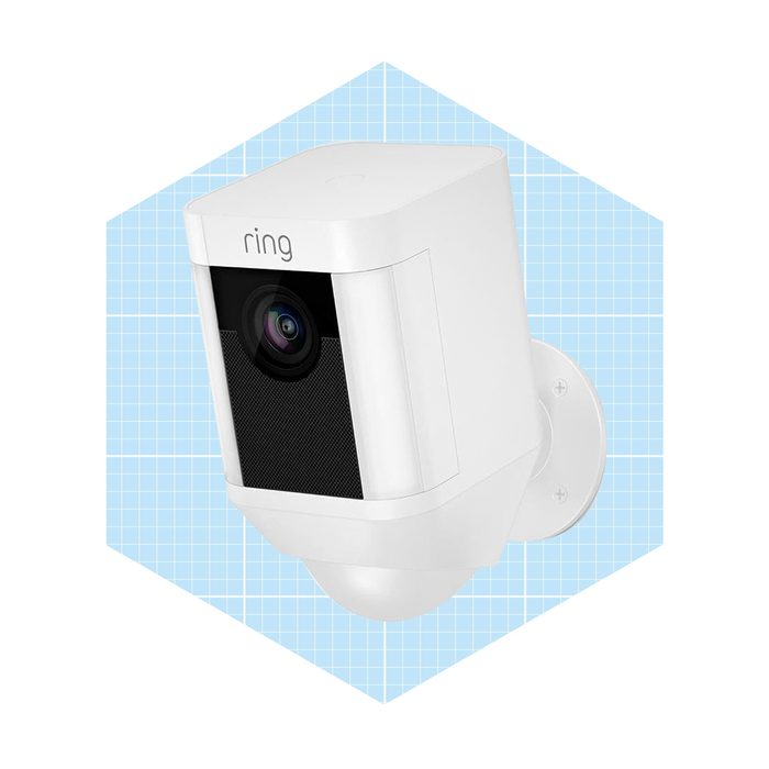 A white security camera is mounted on a wall, capturing its surroundings against a blue grid background, designed for monitoring and providing security.