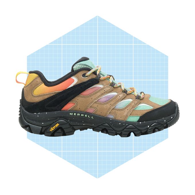 A hiking shoe is displayed on a light blue grid background, showcasing a colorful design with mixed materials and a rugged sole for outdoor use.