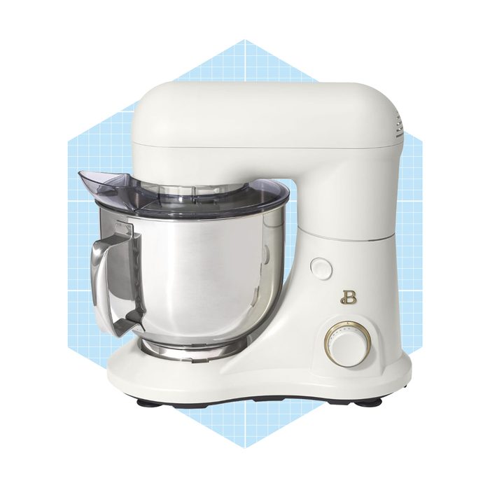A white stand mixer with a stainless steel bowl sits on a flat surface, ready for mixing ingredients against a light blue geometric background.