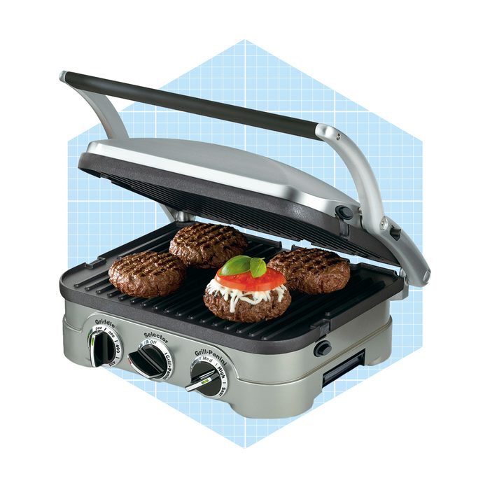 A grill with four cooking patties cooks meat while the lid is closed. It features adjustable temperature dials and is set against a light blue background.