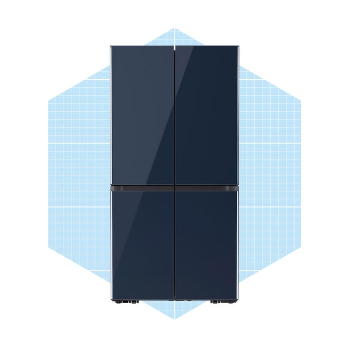 A dark, modern refrigerator stands upright, showcasing its sleek design against a light blue grid-patterned background. The fridge features four doors for storage.