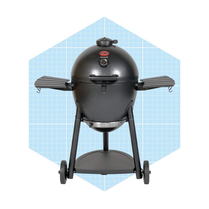 A black, round charcoal grill stands upright, featuring two side shelves and a stable base with wheels, against a light blue grid background.