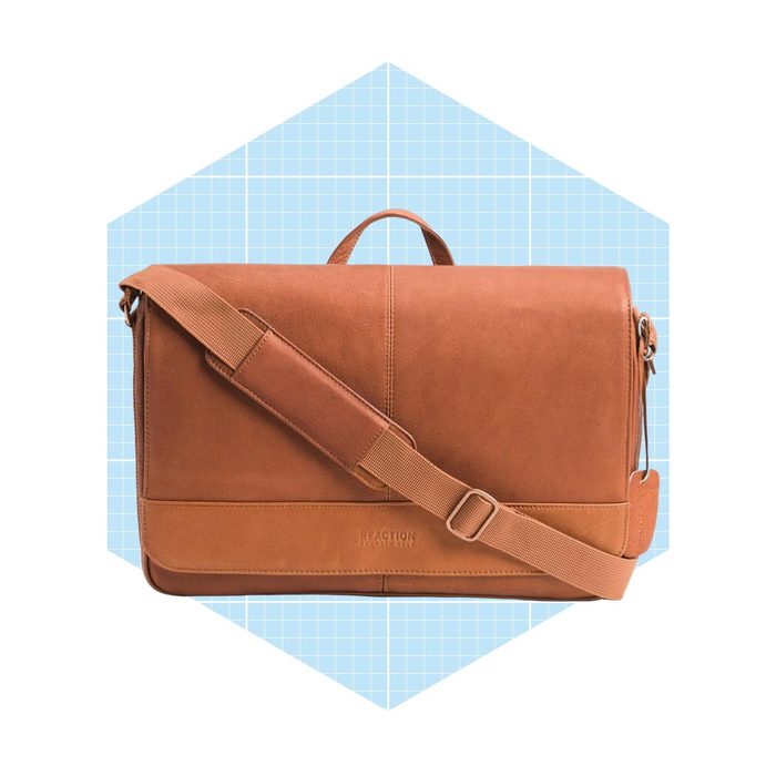A brown leather messenger bag rests on a light blue grid background, featuring a shoulder strap and a top handle for carrying.