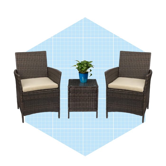 Two wicker chairs with cushions face each other across a small table, topped with a potted plant, set against a light blue grid background.