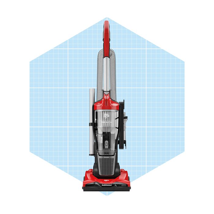 A red upright vacuum cleaner stands vertically, featuring a transparent dust container and flexible hoses, set against a light blue grid background.