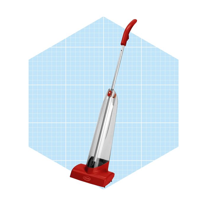 A red upright vacuum cleaner stands upright against a light blue, grid-patterned background, showcasing its sleek design and clear dust container.