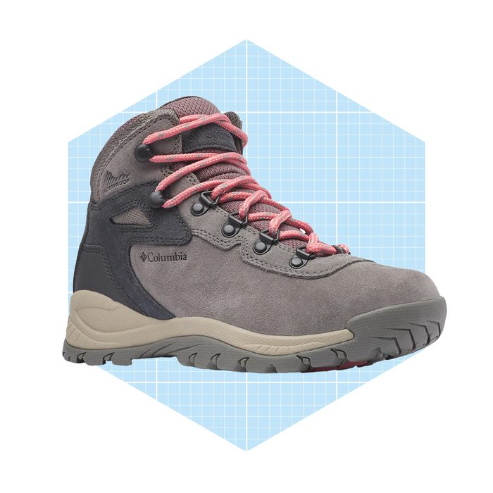 A gray hiking boot with pink laces stands on a light blue grid background, showcasing its rugged sole and waterproof design for outdoor activities.