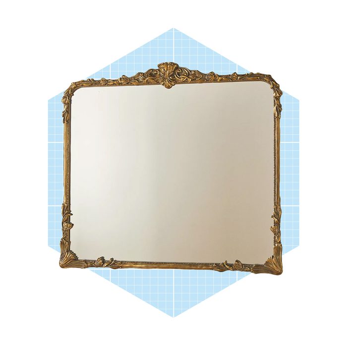 An ornate, gold-framed mirror reflects light, positioned in front of a light blue grid-patterned background, enhancing its decorative appeal.