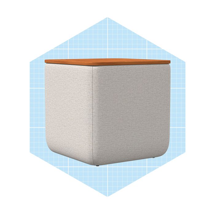 A rectangular upholstered ottoman with a wooden top sits centered against a light blue grid background, suggesting a modern, minimalist design.