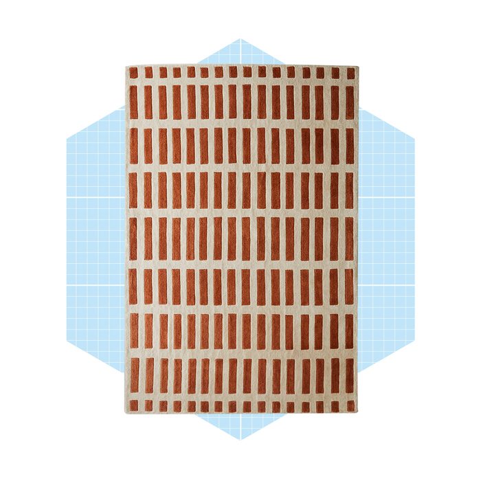 A rectangular rug with a patterned design of alternating brown and cream rectangles lies against a light blue geometric background.