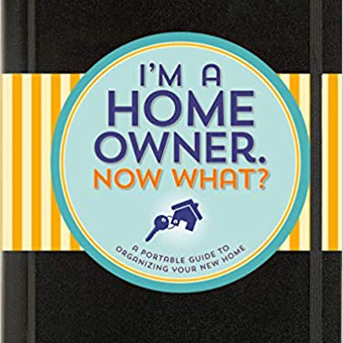 A black notebook features a circular cover with the text “I'M A HOME OWNER. NOW WHAT?” alongside illustrations of keys and a house, against a striped background.