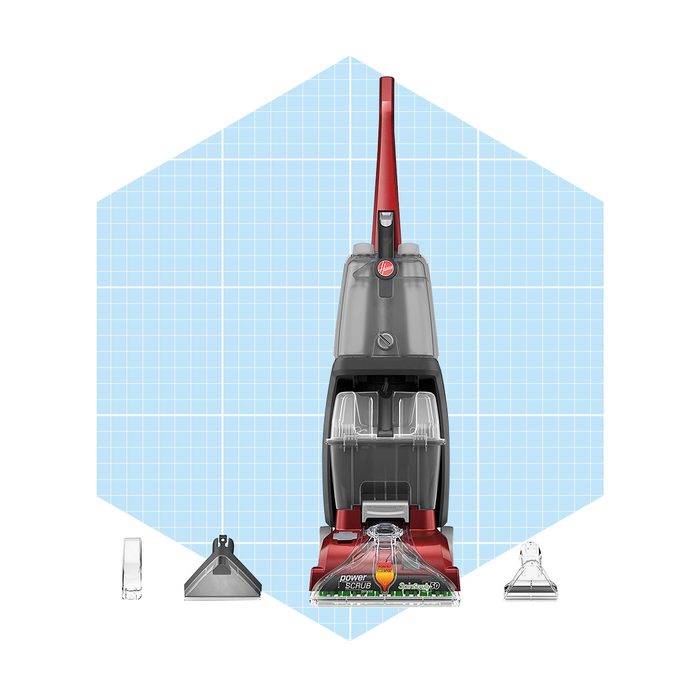 A red and gray carpet cleaner stands upright with attachments beside it, positioned on a blue grid background, ready for cleaning tasks.