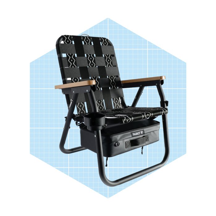 A black folding chair with patterned fabric sits against a light blue grid background, featuring wooden armrests and a storage pouch beneath.