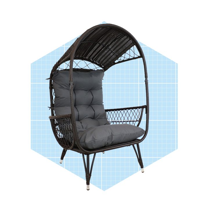 A black, woven chair with a high back and canopy offers spacious seating, featuring plush gray cushions, set against a light blue geometric background.