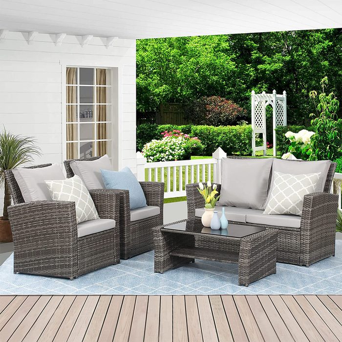 Outdoor seating includes two armchairs and a sofa around a glass-topped table, surrounded by greenery and a white picket fence.