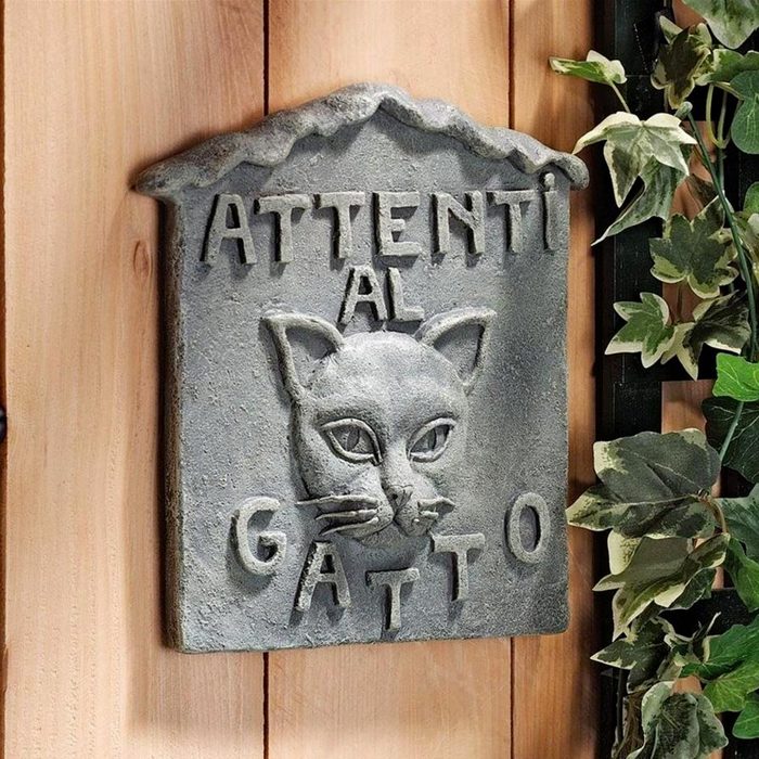 A decorative stone plaque features a carved cat's face. It displays the words, 