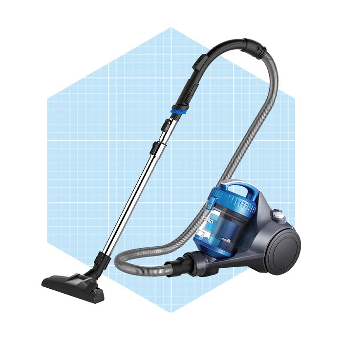 A canister vacuum cleaner stands upright with a flexible hose and wand, set against a light blue grid background, ready for cleaning tasks.