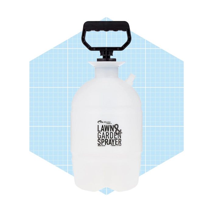 A white plastic lawn and garden sprayer stands upright, equipped with a black handle and a nozzle, set against a light blue grid background.