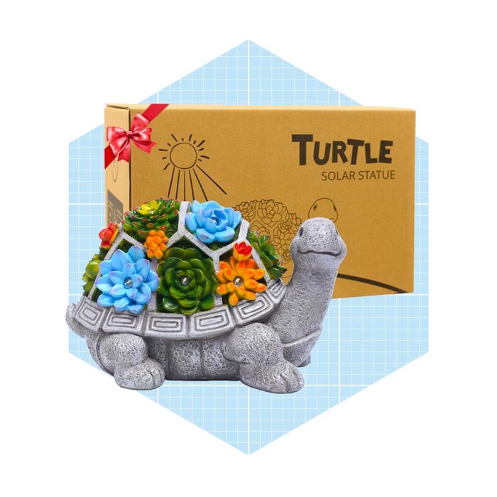 A turtle-shaped statue with colorful, artificial flowers on its back is displayed next to a gift box labeled 