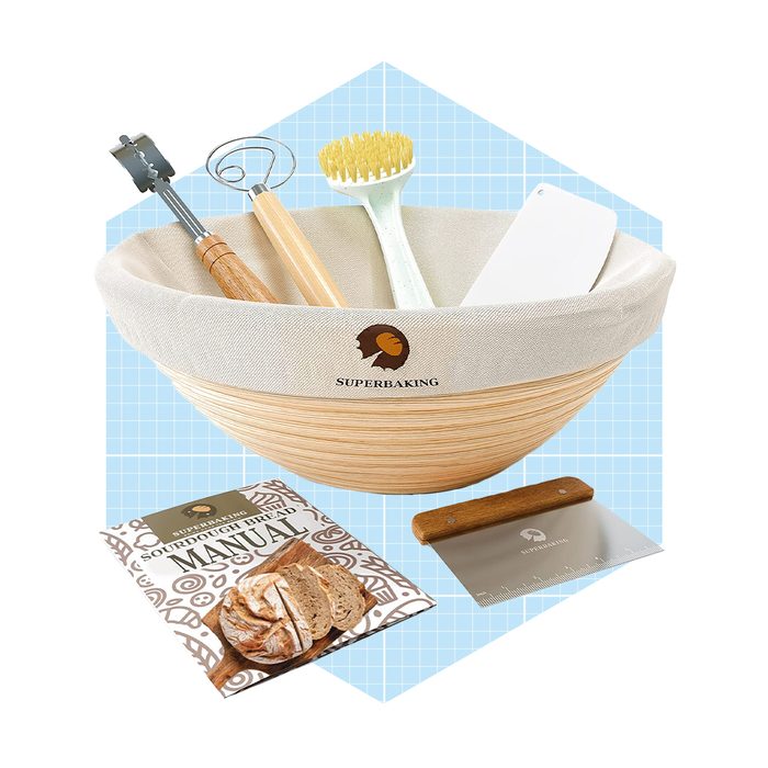 A wooden mixing bowl contains baking tools and a manual, all situated on a light blue grid background, suggesting a baking preparation context.