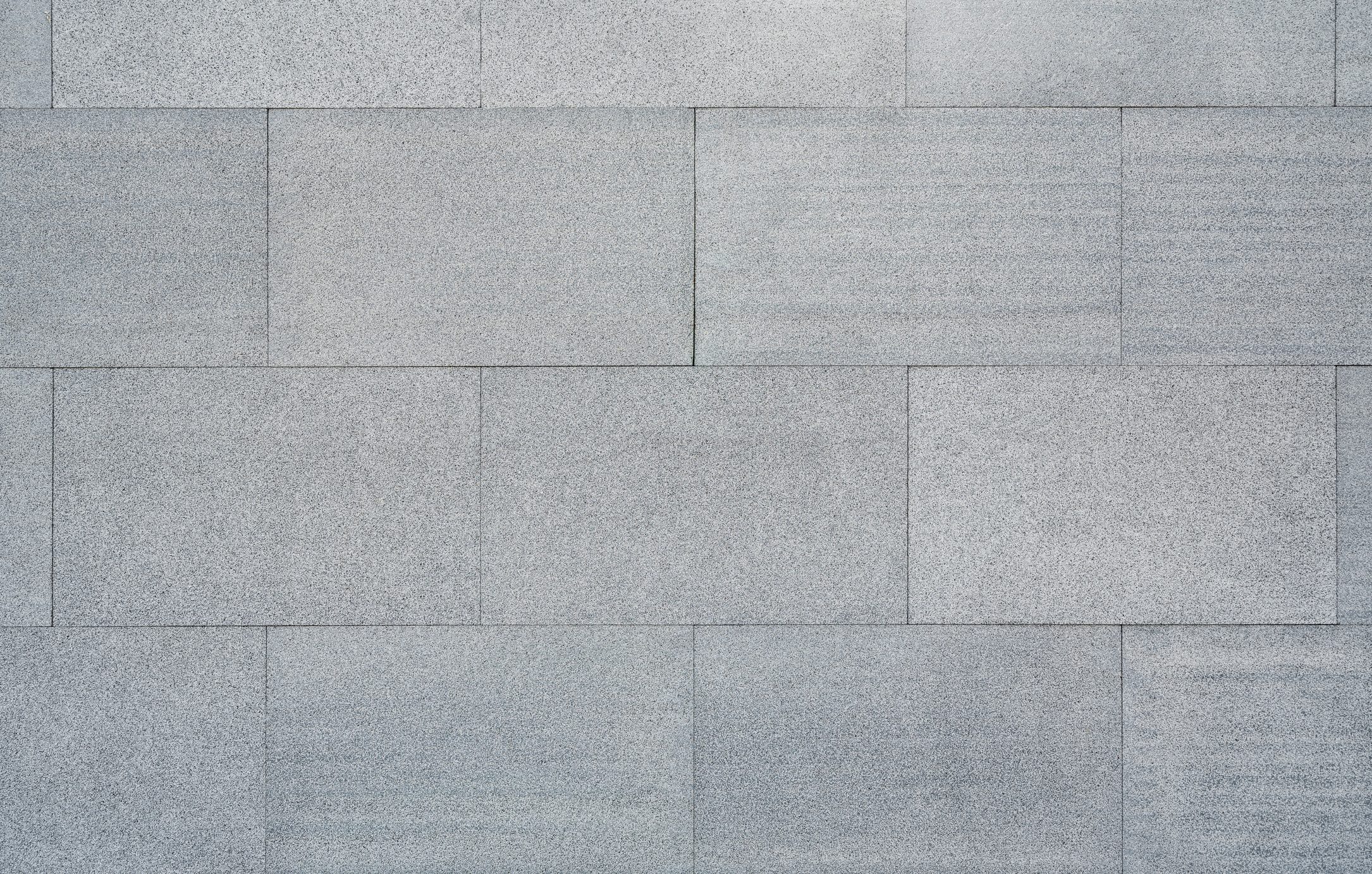 Gray stone tiles are arranged uniformly, creating a smooth surface with slight variations in texture and shade, suitable for walls or flooring.