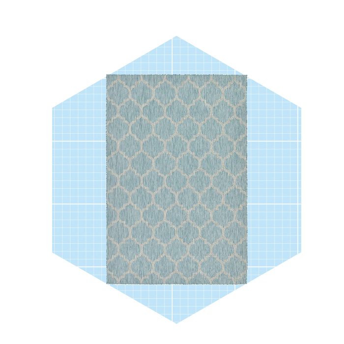 A patterned rug lies flat against a light blue grid background, featuring a decorative design in soft colors, enhancing the visual texture of the scene.