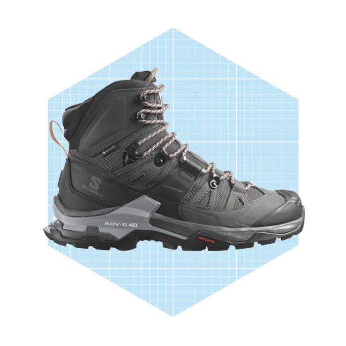 A black hiking boot stands upright, showcasing its lacing system and textured design, set against a light blue, grid-patterned background.