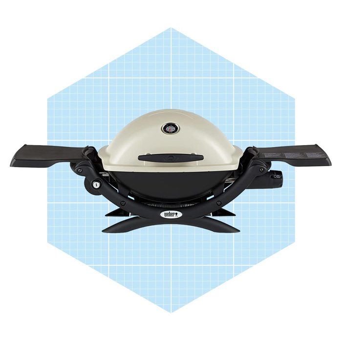 A portable gas grill sits upright, ready for use, with side tables extended and a control knob, against a light blue geometric background.