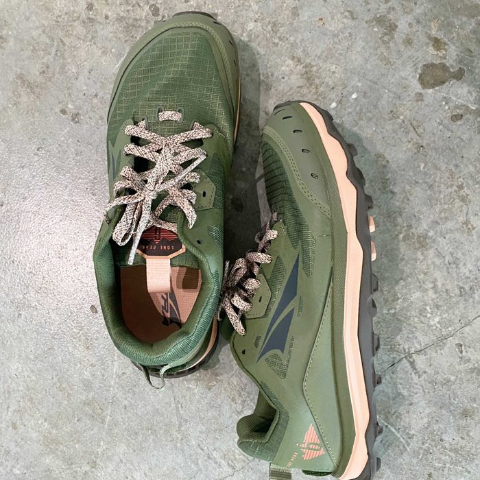 Green athletic shoes with beige soles and gray laces rest on a textured gray surface, featuring a breathable upper design suitable for outdoor activities.