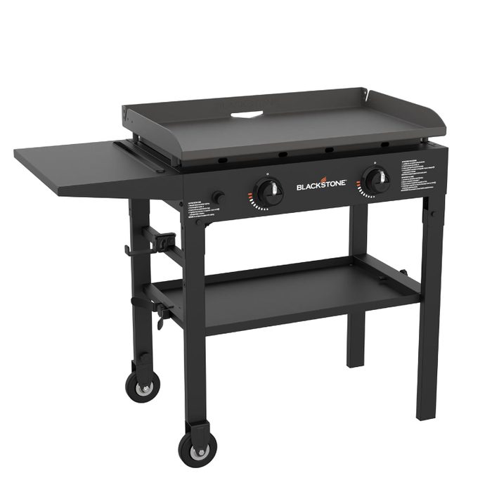 A gas griddle with two knobs on a wheeled cart, featuring a flat cooking surface and a side shelf, designed for outdoor cooking.