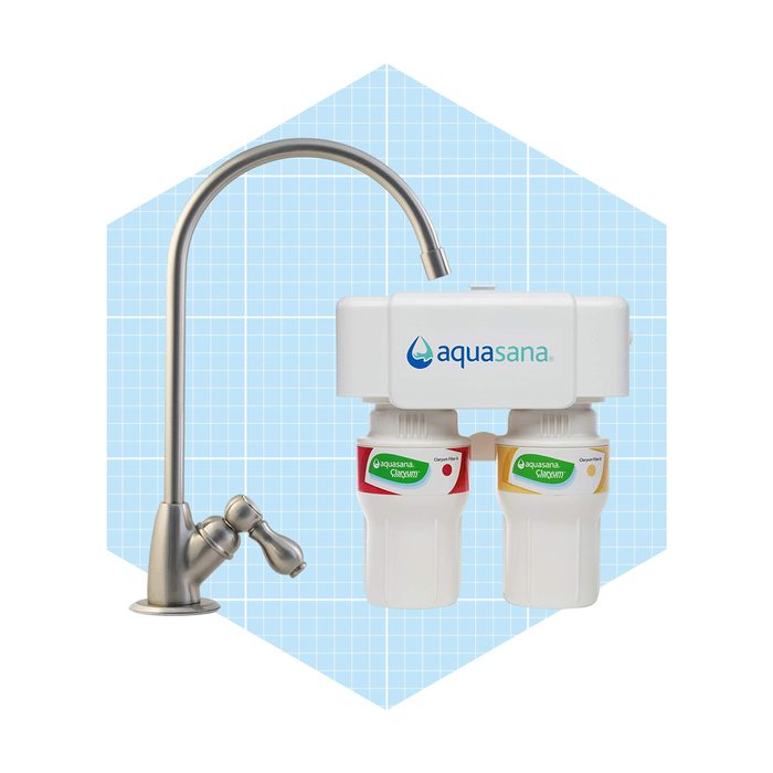 A water filtration system is mounted with a sleek metal faucet, filtering water through two colored cartridges, set against a soft blue background.
