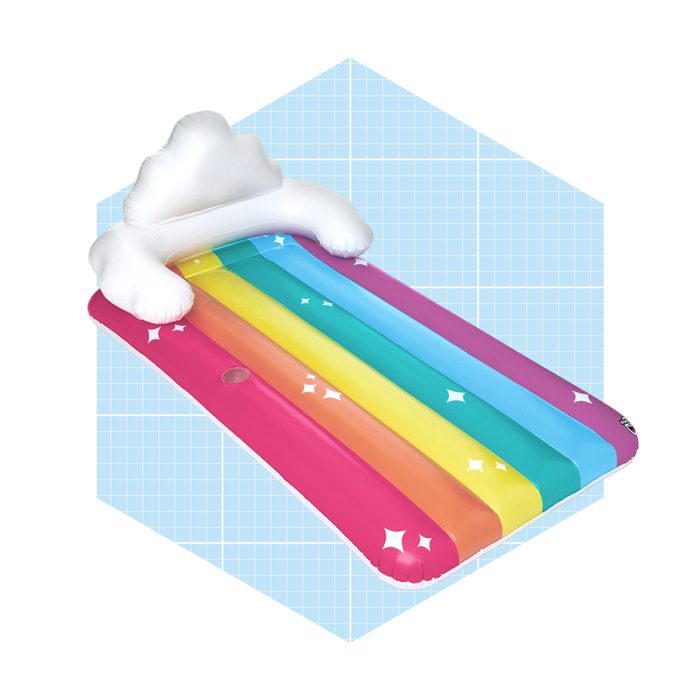 An inflatable rainbow pool float rests against a light blue grid background, featuring a cloud-shaped headrest and sparkling star designs.