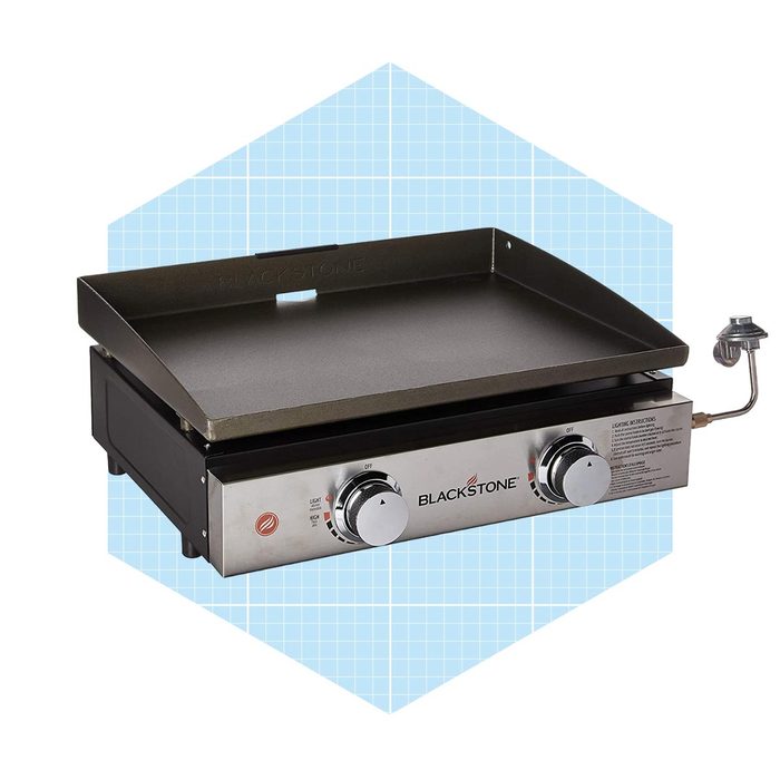 A Blackstone griddle sits on a surface, featuring a large flat cooking area and two control knobs for adjusting heat levels against a light blue background.