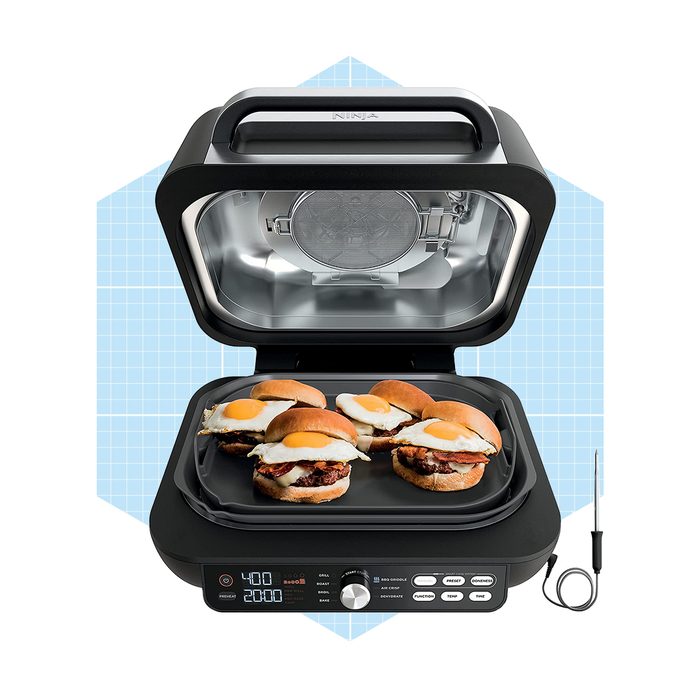 A grill cooker is preparing sandwiches with fried eggs inside a kitchen setting, featuring a digital display and a transparent lid.