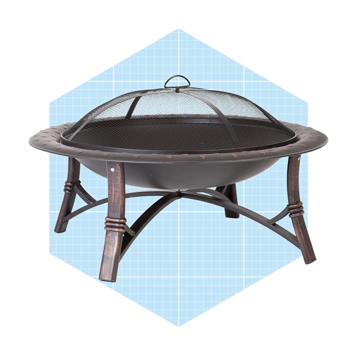 A round fire pit rests on four wooden legs, covered by a mesh spark guard, set against a light blue geometric background.