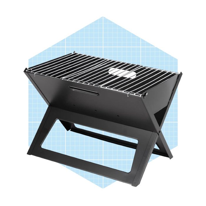 A portable black grill sits on a blue geometric background, featuring a slatted cooking surface and a foldable design for easy storage and transport.