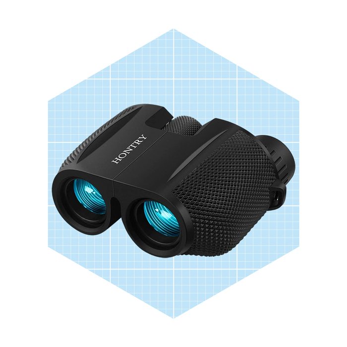A pair of black binoculars rests on a light blue grid background, featuring textured grips and blue lenses, designed for observing distant objects.