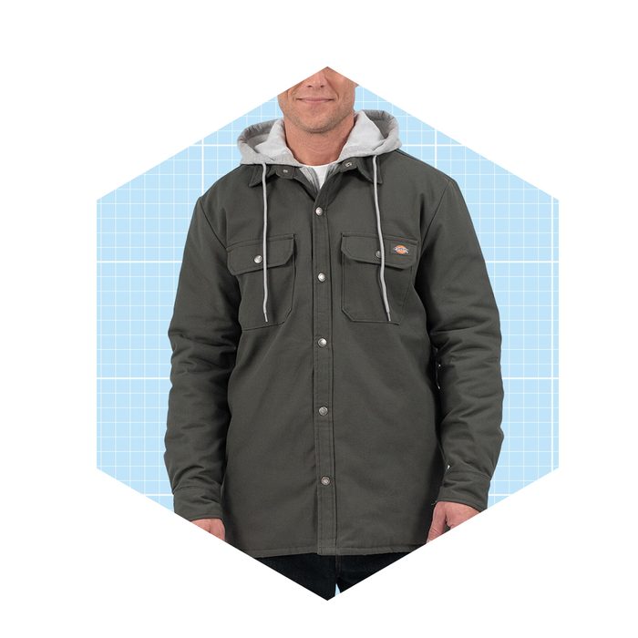 A man is wearing a dark green jacket with a gray hood, standing against a light blue grid background.