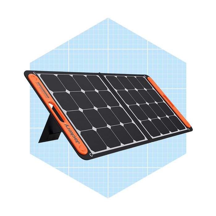 A portable solar panel is open for use, positioned upright on a surface against a grid-patterned light blue background, designed for charging devices outdoors.