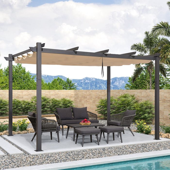 A patio set with black furniture rests under a canopy, surrounded by greenery and mountains, beside a paved area next to a pool.