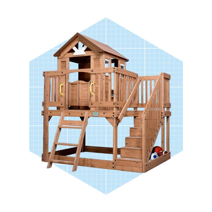 A wooden playhouse with a balcony and slide features stairs and colorful balls underneath, set against a light blue grid background.