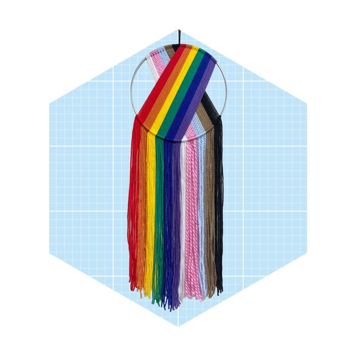 A circular hoop displays strands of colorful yarn, arranged in a rainbow pattern alongside various solid colors, set against a light blue grid background.