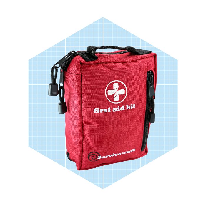 A red first aid kit stands upright, with a zipper and a handle on top, against a light blue grid-patterned background.