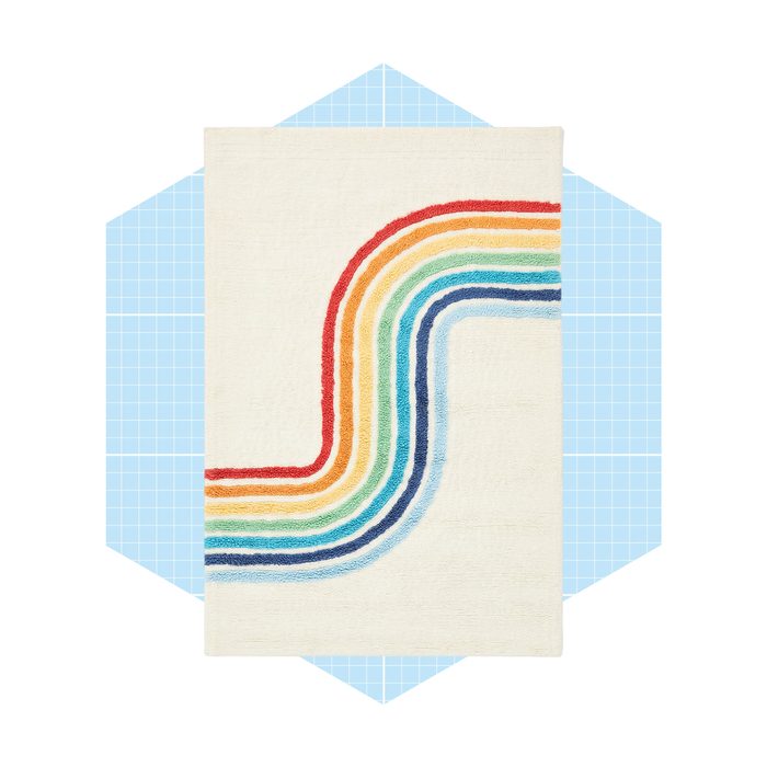A rectangular rug features multicolored, wavy lines against a light background, placed on a blue, grid-patterned backdrop.