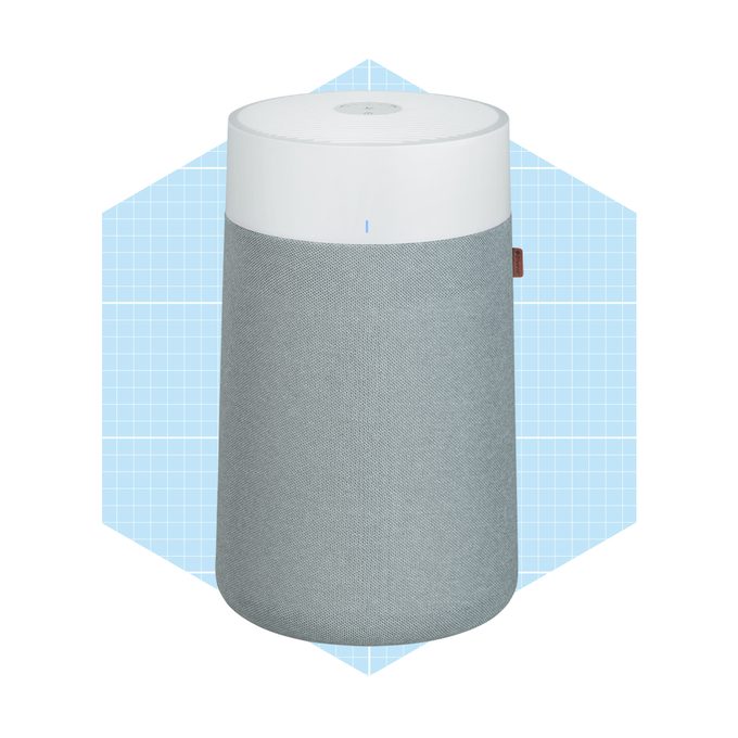 A cylindrical smart speaker with a gray fabric exterior and white top sits against a light blue geometric background, designed for audio playback.